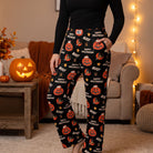Person wearing black Snoopy Halloween lounge pants with jack-o-lantern prints while standing in a cozy living room.