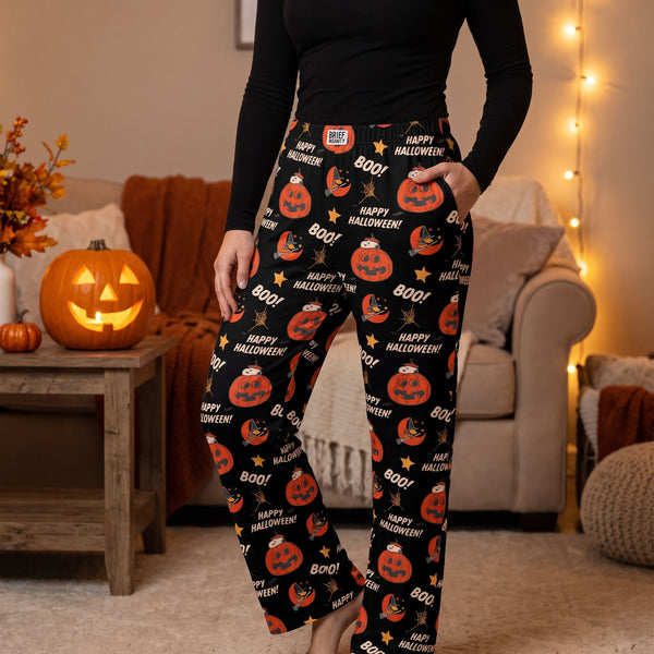 Person wearing black Snoopy Halloween lounge pants with jack-o-lantern prints while standing in a cozy living room.