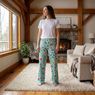 Model standing in cozy rustic living room wearing Snoopy camping-pattern lounge pants, showcasing relaxed fit and lightweight fabric.
