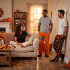 Three models wearing Snoopy themed Halloween lounge pant sets in a cozy living room decorated with fall pumpkins and leaves.