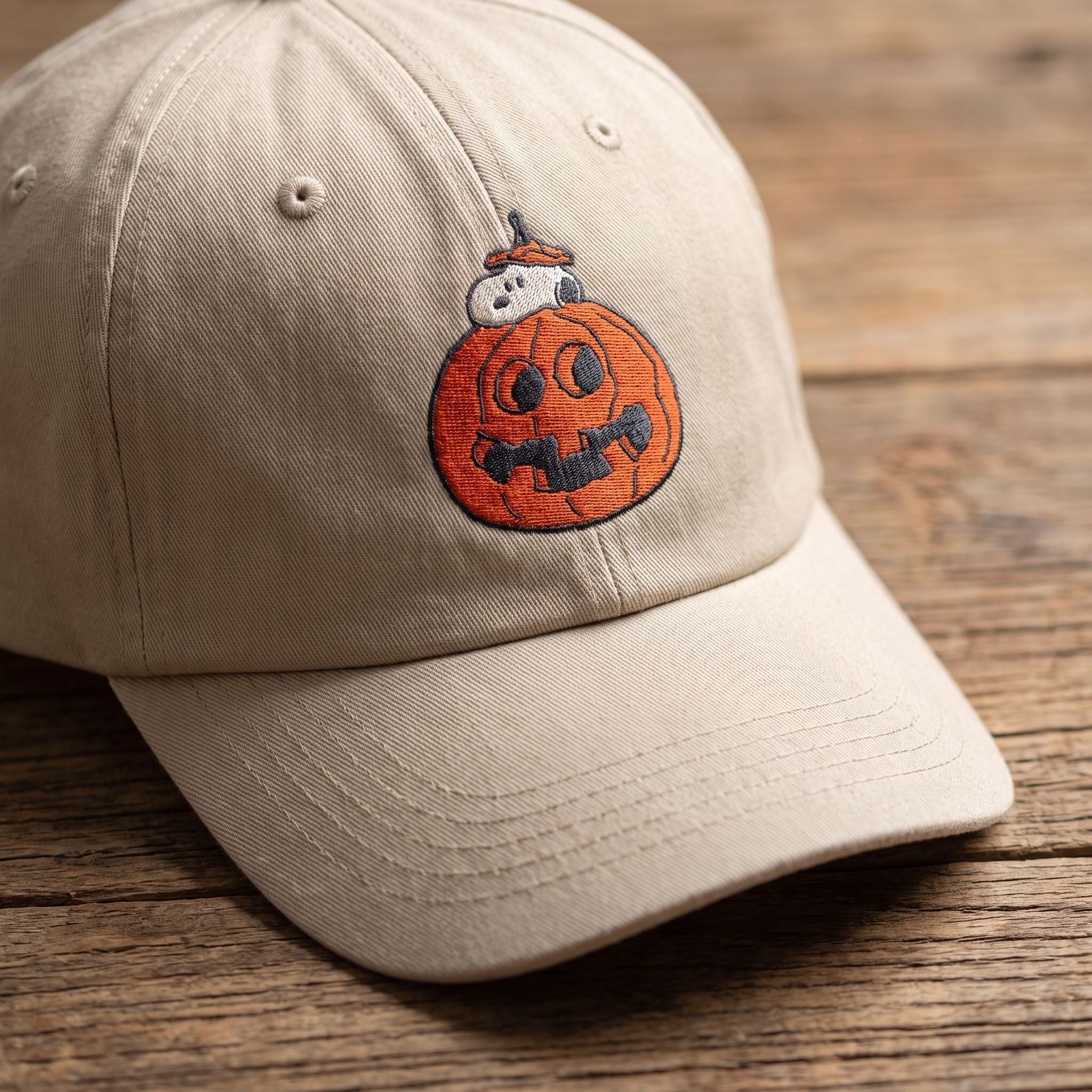 Close-up of Snoopy in a pumpkin embroidered cap on a wooden surface, showing detailed embroidery and fabric texture.