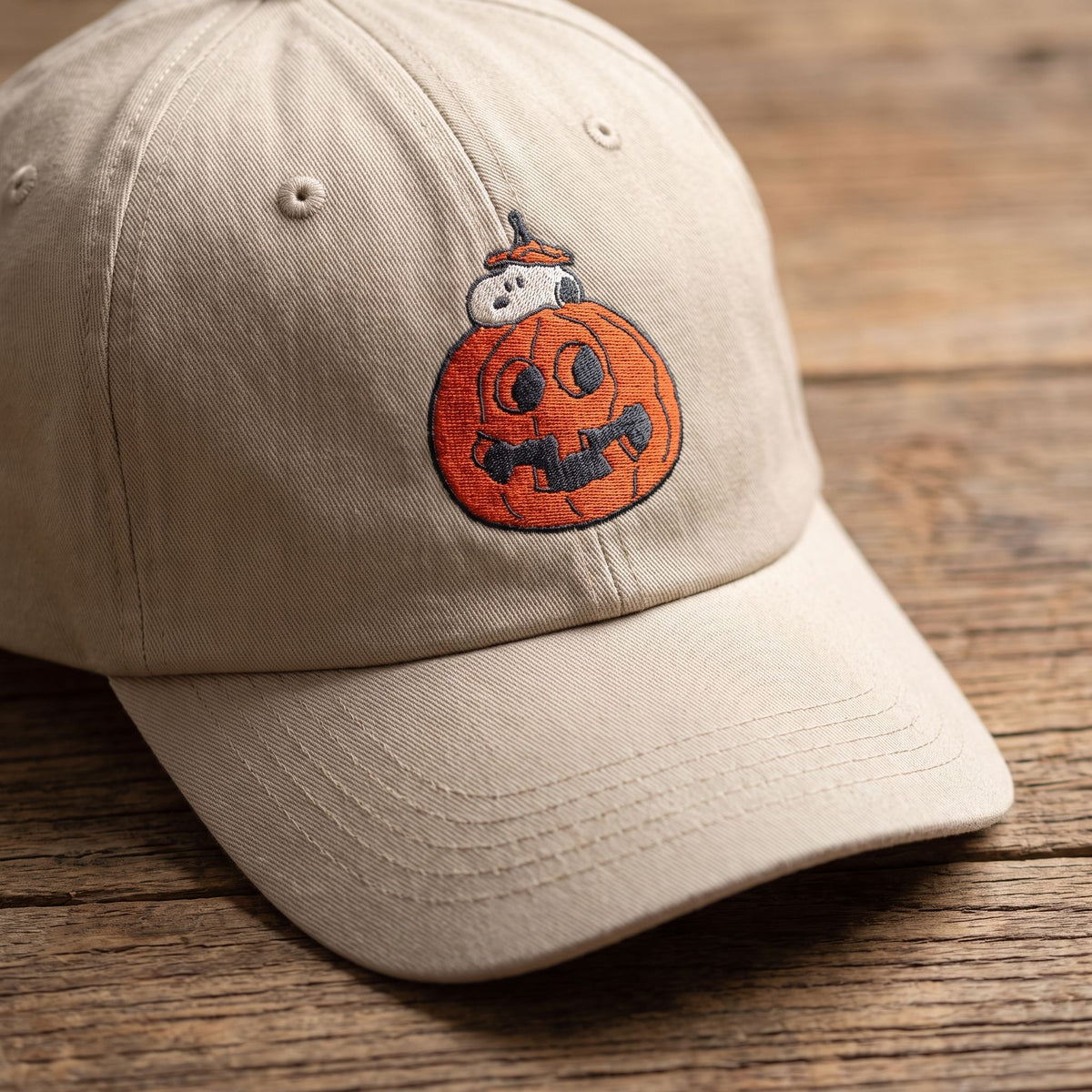 Close-up of Snoopy in a pumpkin embroidered cap on a wooden surface, showing detailed embroidery and fabric texture.