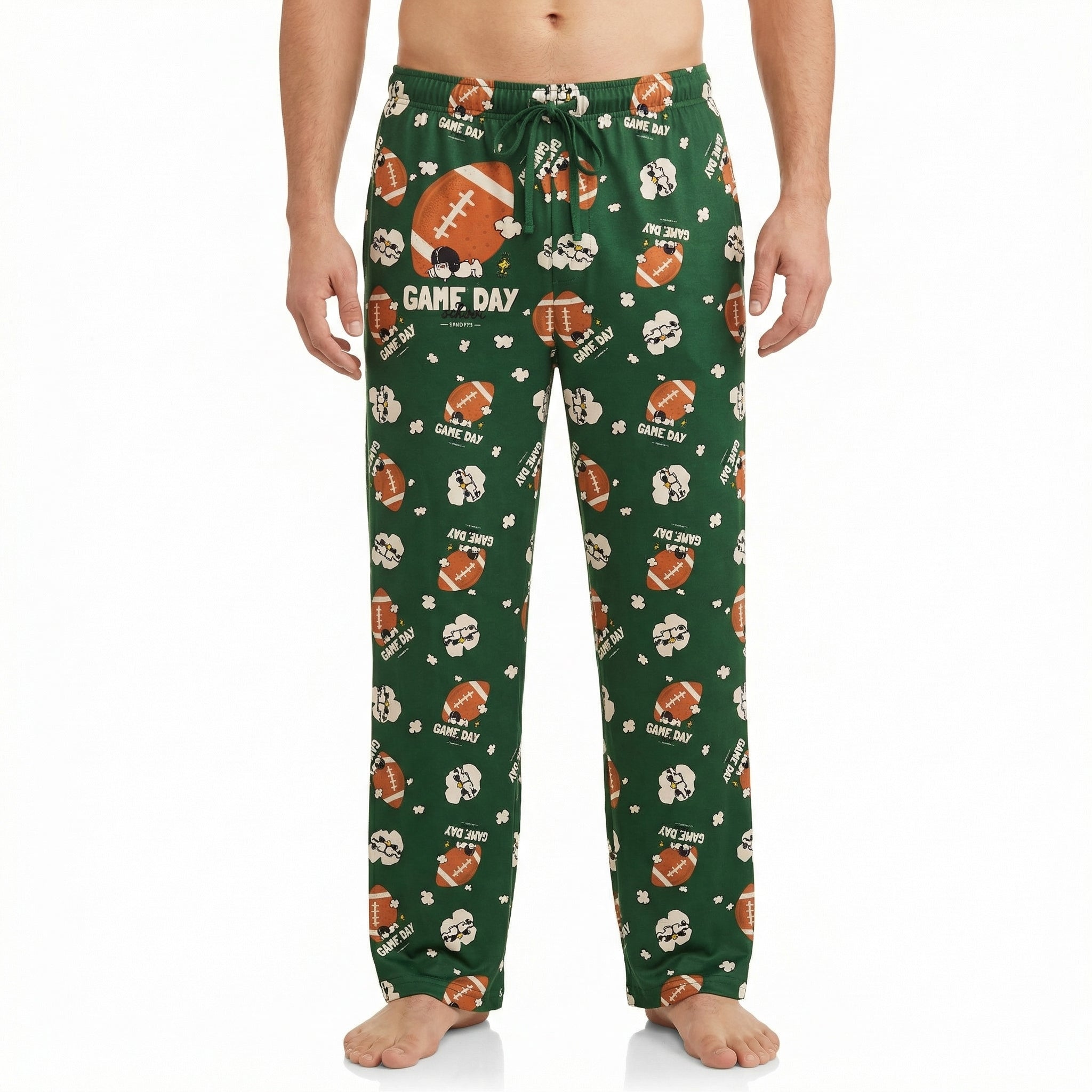 Model wearing green football-themed lounge pants featuring Snoopy and game day graphics, cropped from waist to ankles against white background.