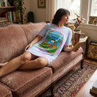 Person lounging on a vintage sofa in a cozy living room wearing Peanuts Lucy's psychiatric retreat night shirt showing pastel tie-dye colors and relaxed fit.