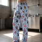 Model wearing Wizard of Oz lounge pants featuring iconic characters and gingham pattern in an industrial style kitchen.