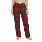 Young female model standing confidently in a lively living room, wearing red plaid pajama pants, surrounded by plants and playful decor.