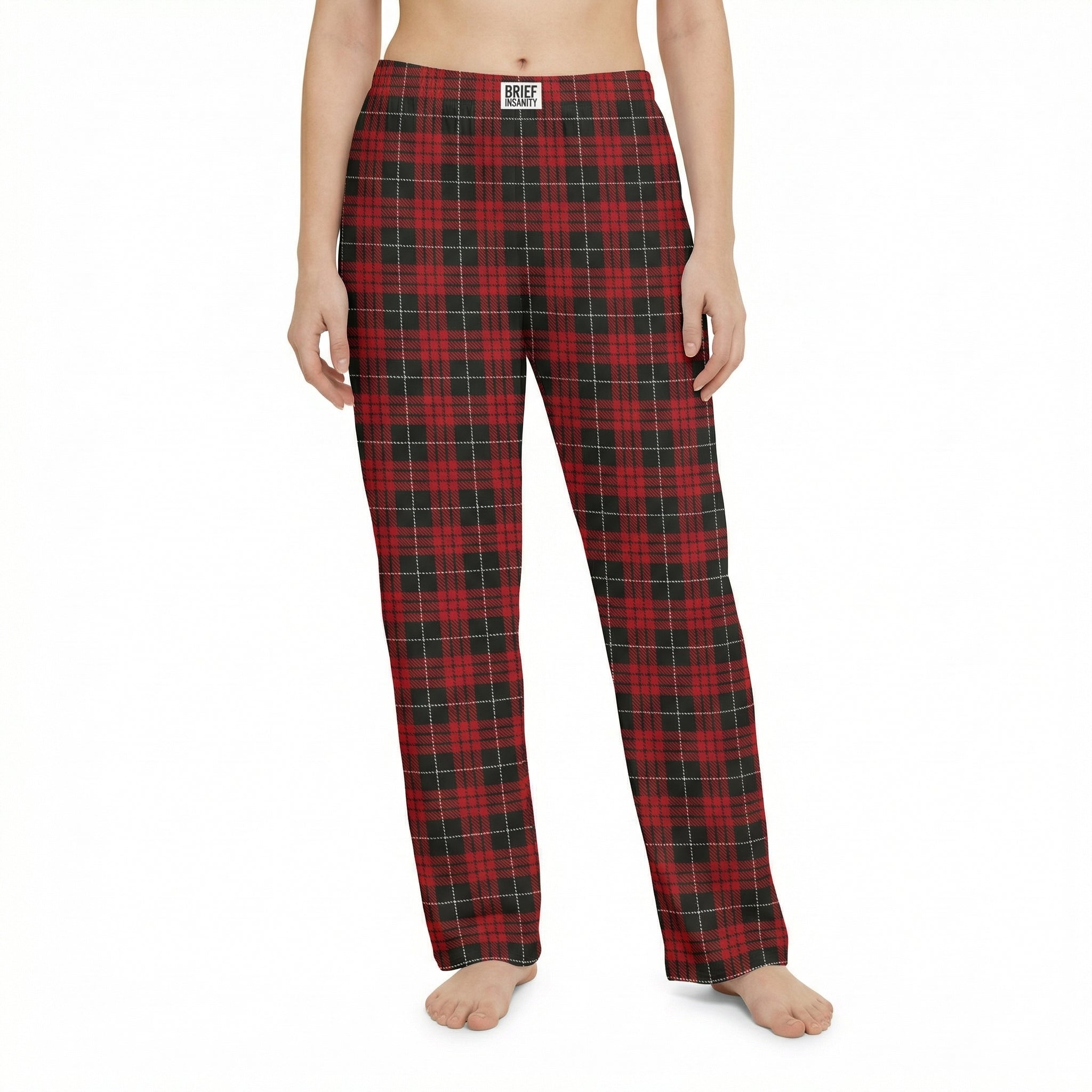 Young female model standing confidently in a lively living room, wearing red plaid pajama pants, surrounded by plants and playful decor.