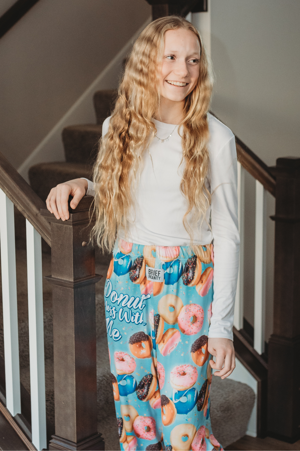 Image of girl model holding on to edge of stairs looking off into the distance smiling and wearing Donut Mess With Me pajama lounge pants (front view)