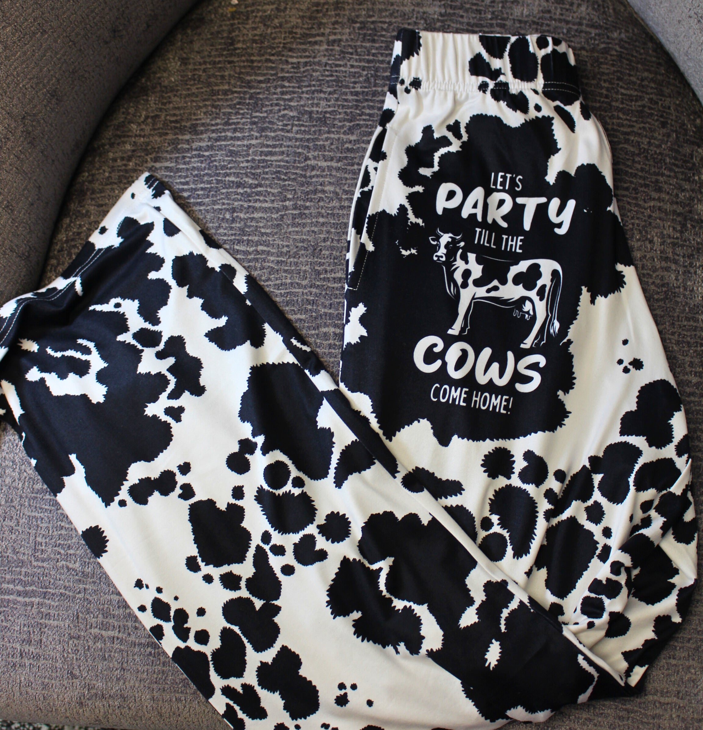 Party 'Till The Cows Come Home pajama lounge pants laid out on a gray chair