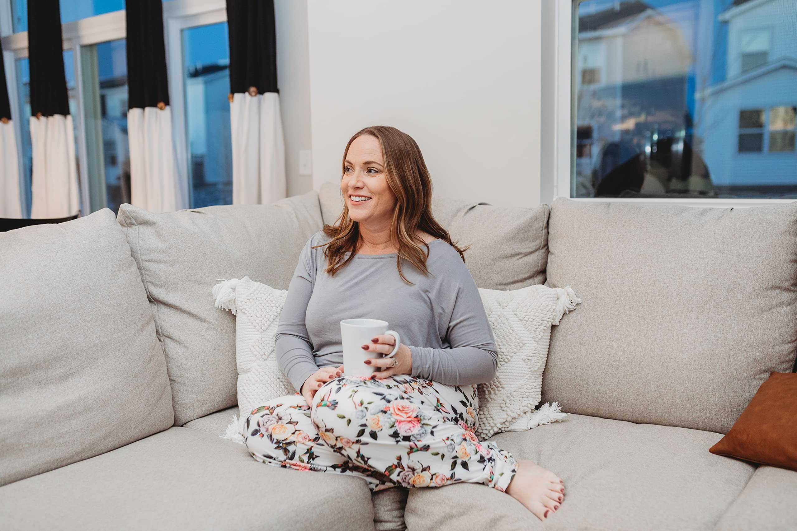 Image of female model sitting on a gray couch looking off into the distance smiling wearing Hummingbird Pattern pajama lounge pants