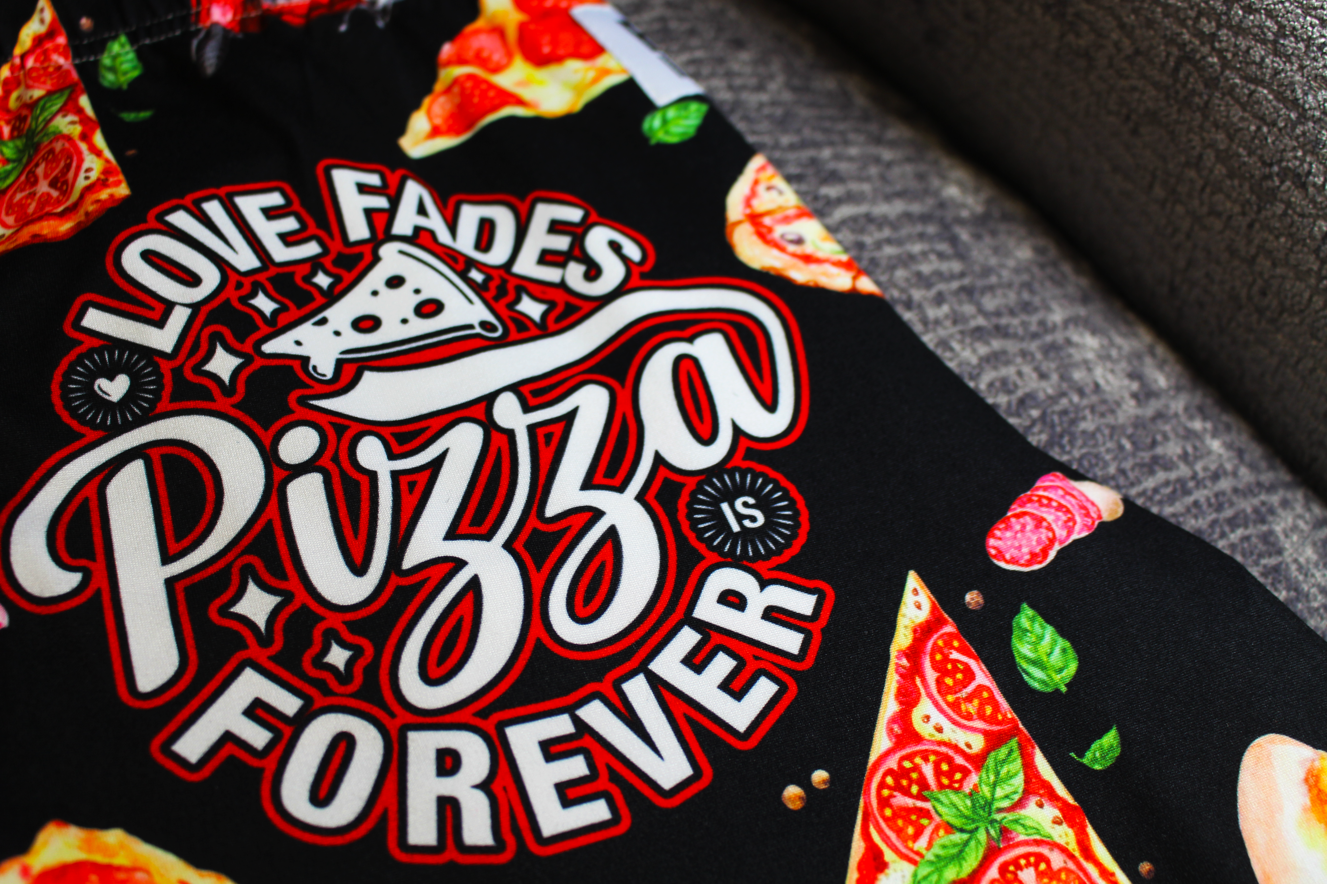 Pizza Is Forever pajama lounge pants laid out on gray chair close up image of text