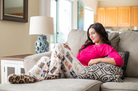 Image of female model sitting on a gray couch with knees up wearing Check Meowt pajama lounge pants (side view)