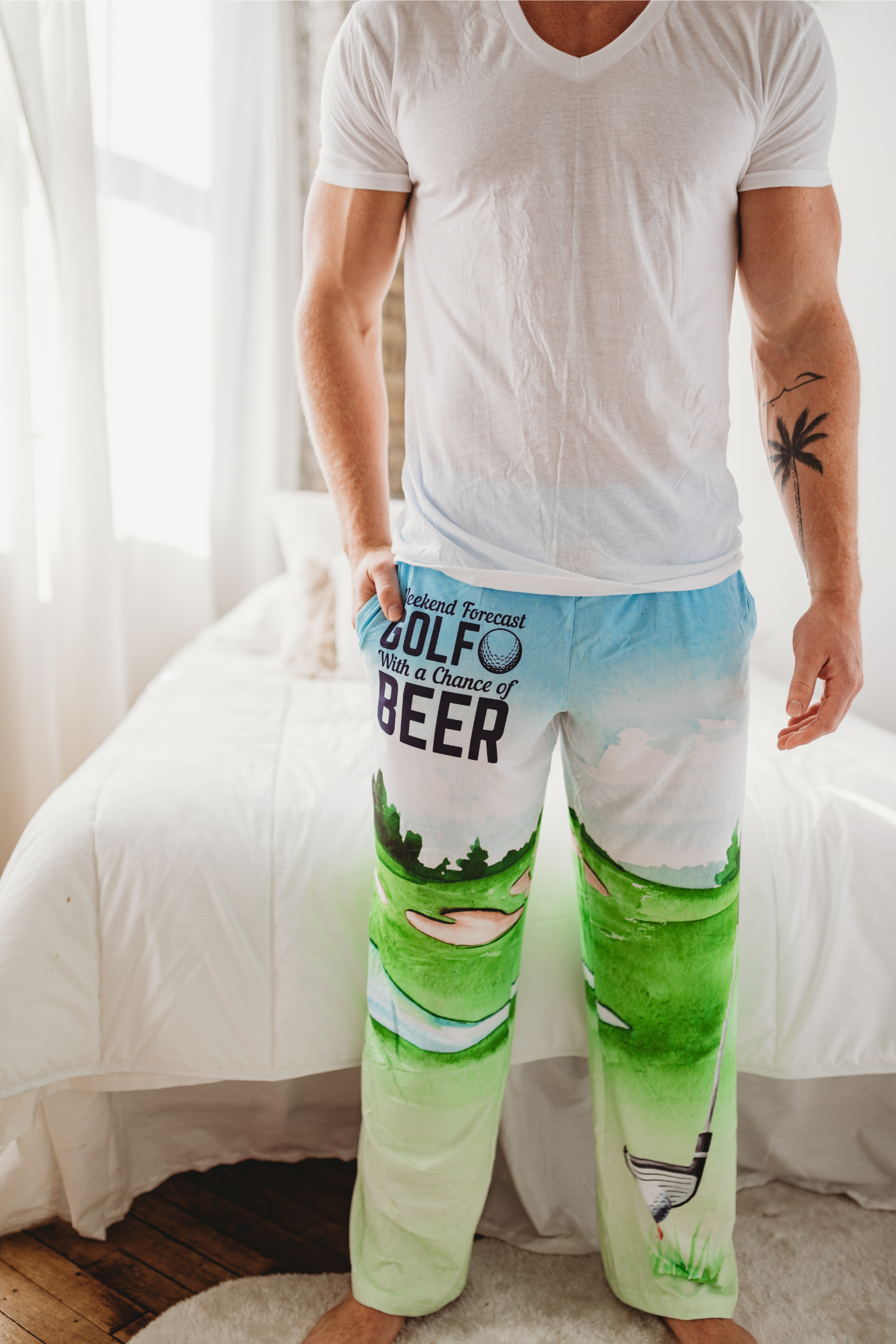Male model standing in front of white bed wearing Golf With A Chance Of Beer pajama lounge pants (front view)