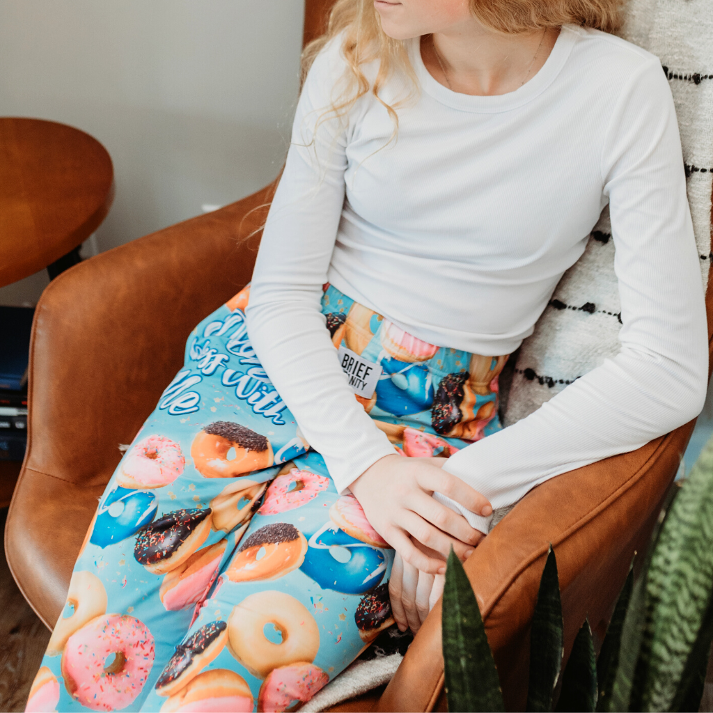 Image of girl model sitting in a lounge chair wearing Donut Mess With Me pajama lounge pants (front view)