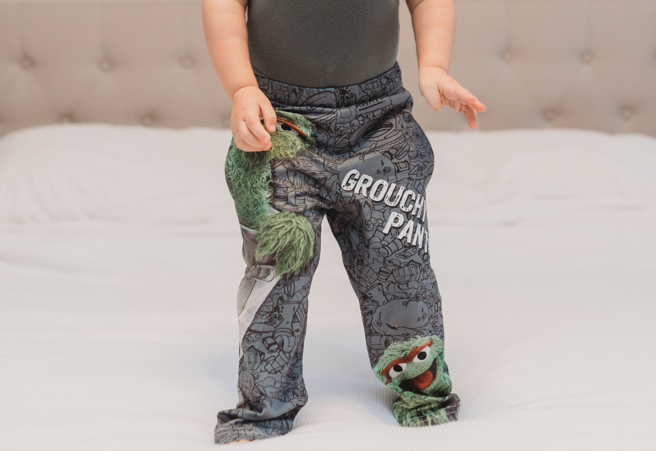 Cropped image of little girl model standing on bed wearing Sesame Street Oscar The Grouch pajama lounge pants (front view)