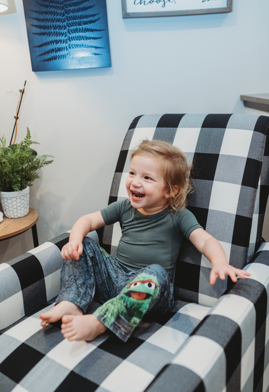 Image of little girl model sitting on a plaid couch giggling wearing Sesame Street Oscar The Grouch pajama lounge pants 